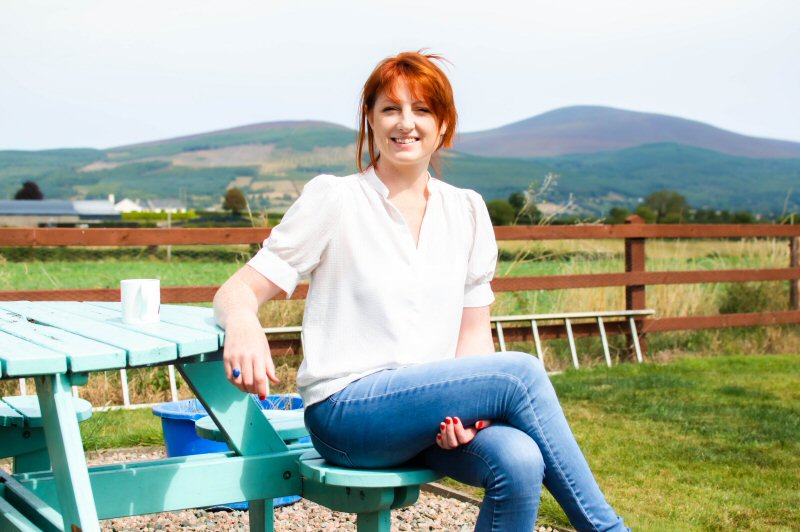 Amy Hill seated at a garden bench outside her home office. To contact me, use the e-mail address or form on this page.